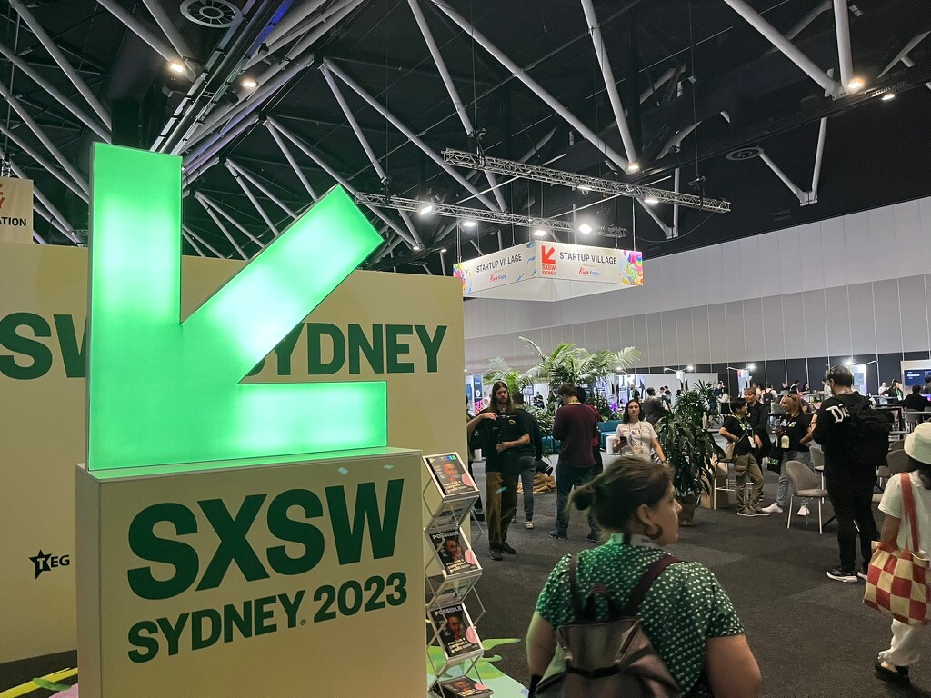 The SXSW Sydney 2023 logo, at the front of a large exhibition hall.