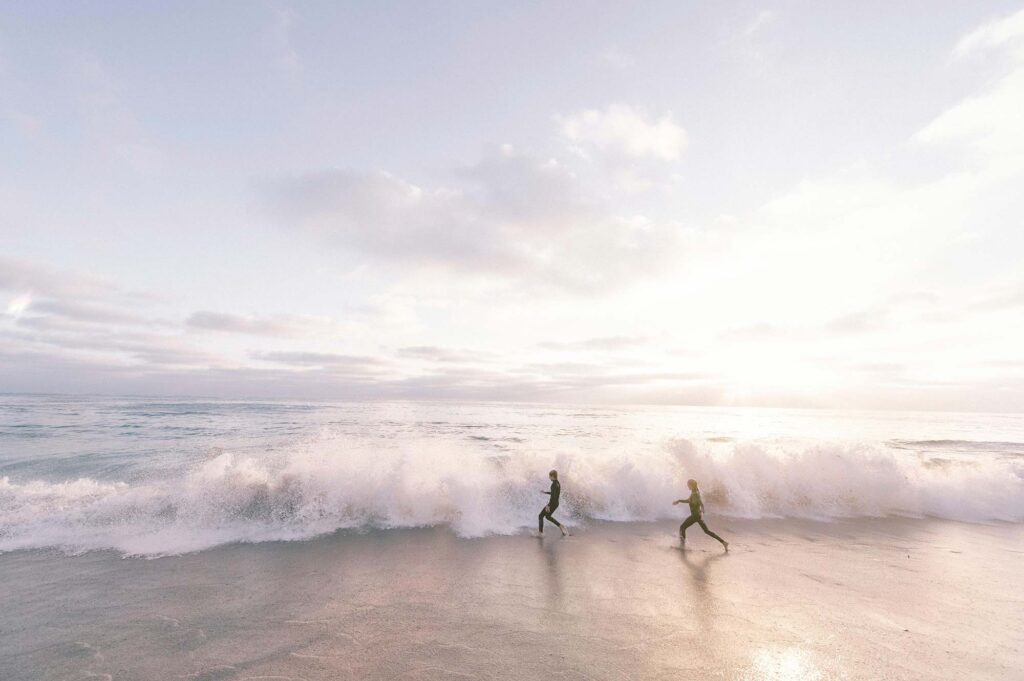 Two people running along the coast in wetsuits
