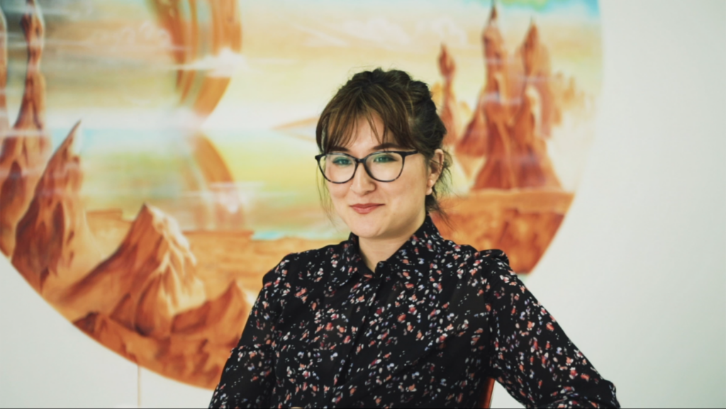 Woman in glasses smiling with scenic painting in background