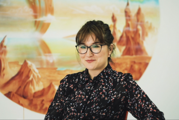 Woman in glasses smiling with scenic painting in background