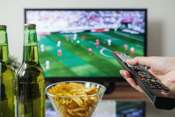 Sports game on television with beers and chips on coffee table, remote in hand